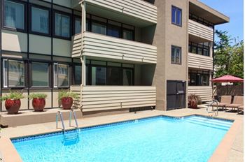 A swimming pool in front of a building with a red umbrella.